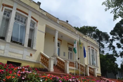 Prédio histórico com jardim e bandeiras na fachada.